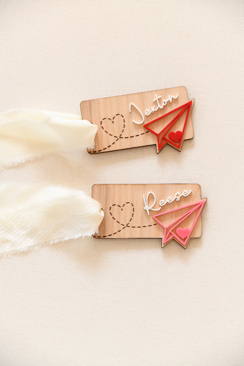 Custom name wood and acrylic Valentines Day name tag. Paper airplane leaving a heart path behind it. With elegant white ribbon to tie to any item or gift.
