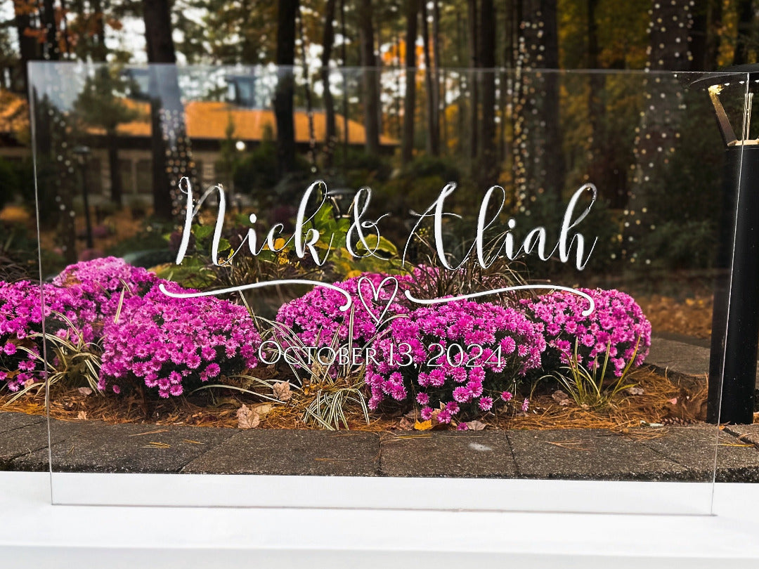 Custom acrylic clear wedding sign with the bride and grooms name and date with a delicate heart to accent the names.